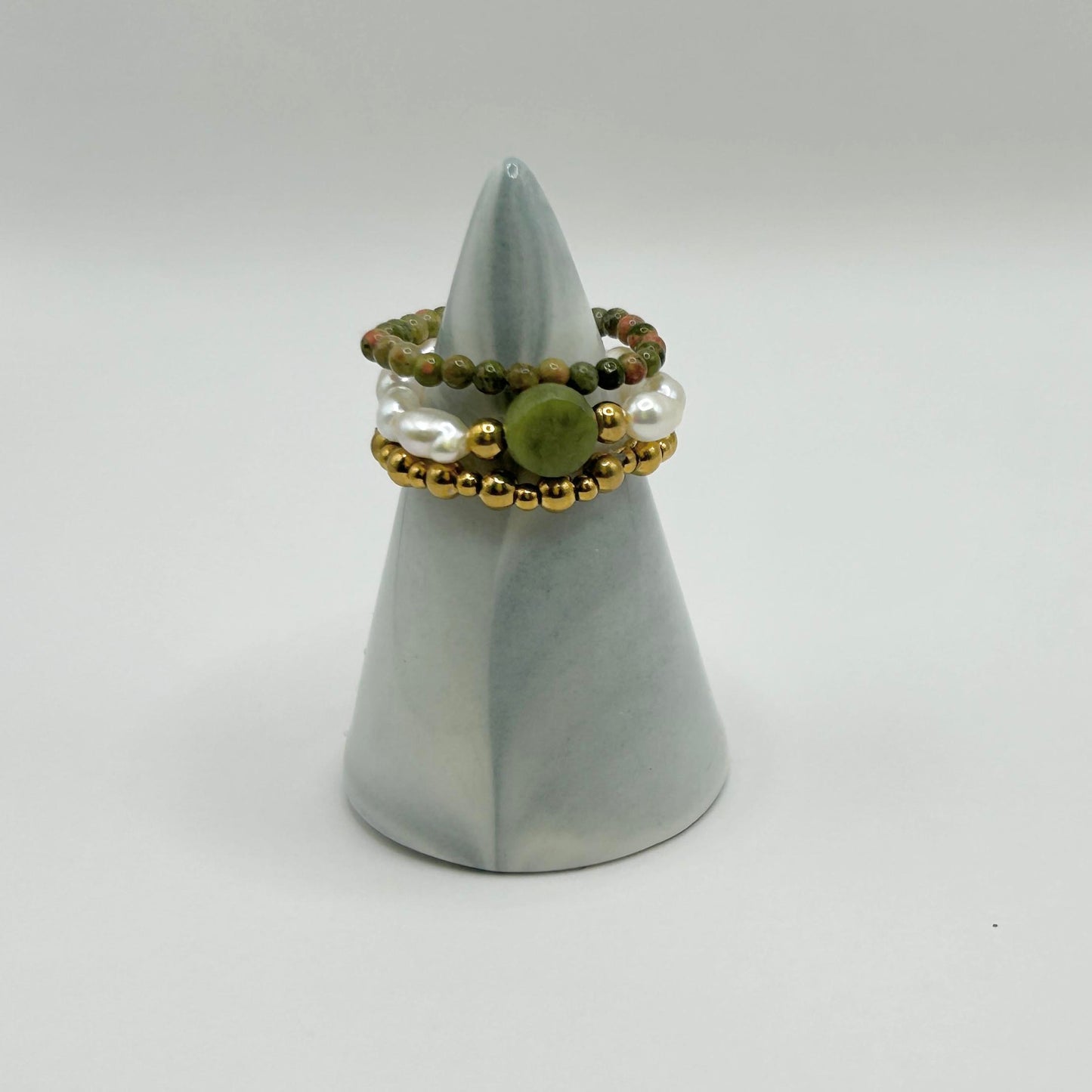 Leopoldine Amity ring trio with green jade, pearls and gold beads, displayed on a minimalist grey cone jewellery holder.