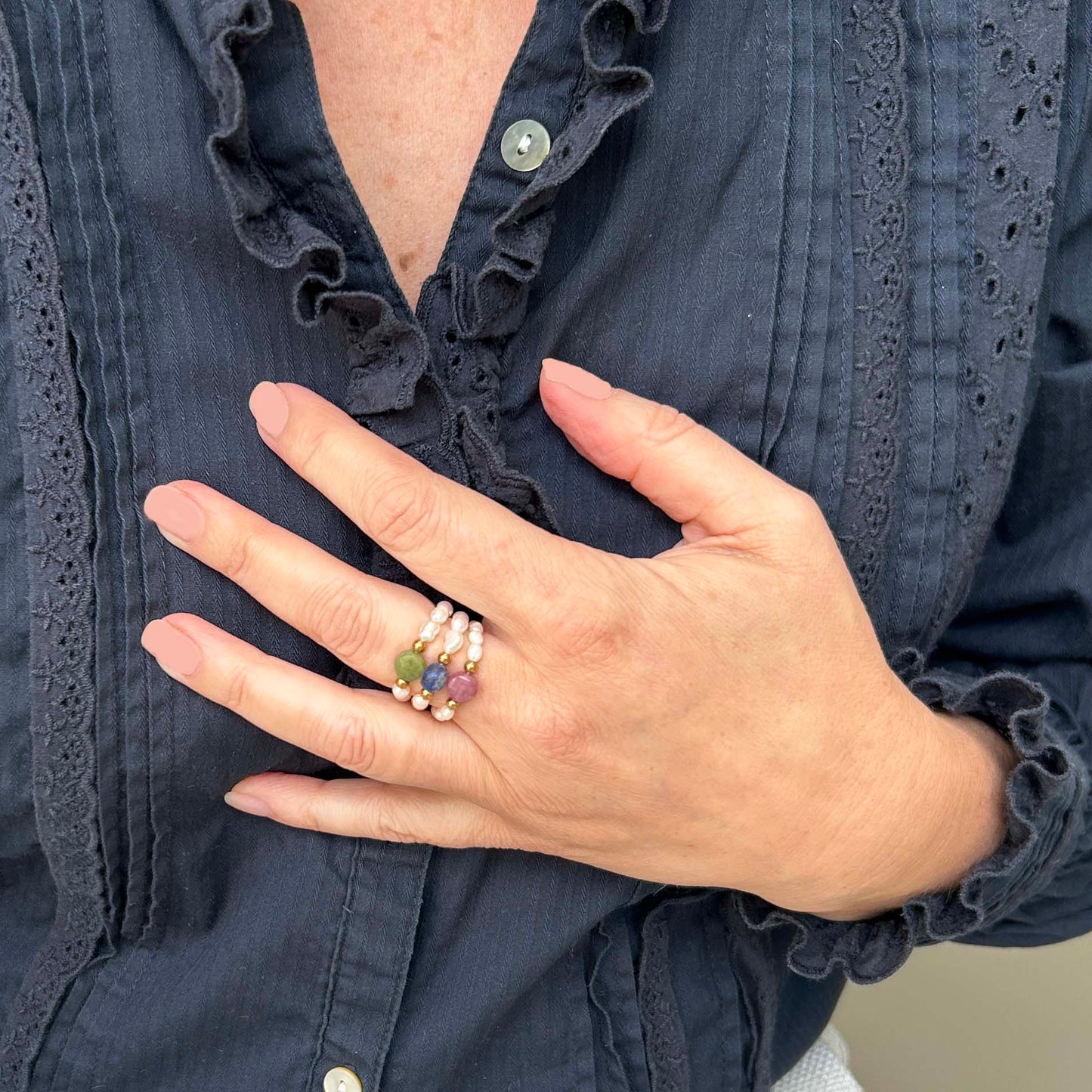 Woman’s hand adorned with colourful gemstone ring trio featuring pink tourmaline, green jade, and blue lapis lazuli beads on elastic bands. A stylish and cheerful accessory stack for a relaxed and feminine UK look.