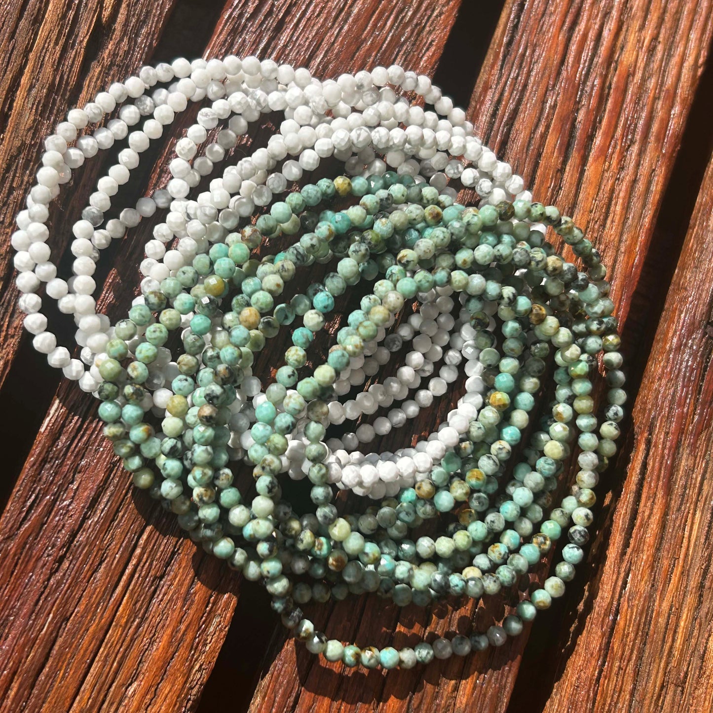 Stack of white and green african turquoise gemstone beaded bracelets displayed on rustic wooden surface – boho-chic handcrafted jewellery perfect for layering.