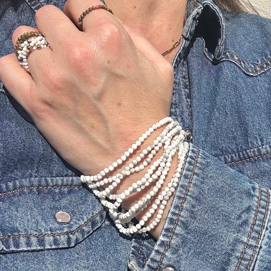 Close-up of hand wearing stacked Aurora white turquoise gemstone ringsand matching gaia bracelets, styled with a denim jacket – elegant boho jewellery for everyday wear.