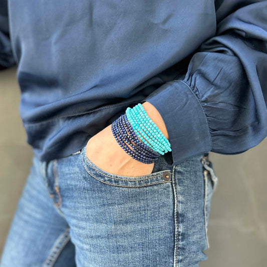 Wrist adorned with layered lapis lazuli and turquoise bead bracelets – vibrant gemstone stack styled with denim jeans and navy top for a fresh, modern look.