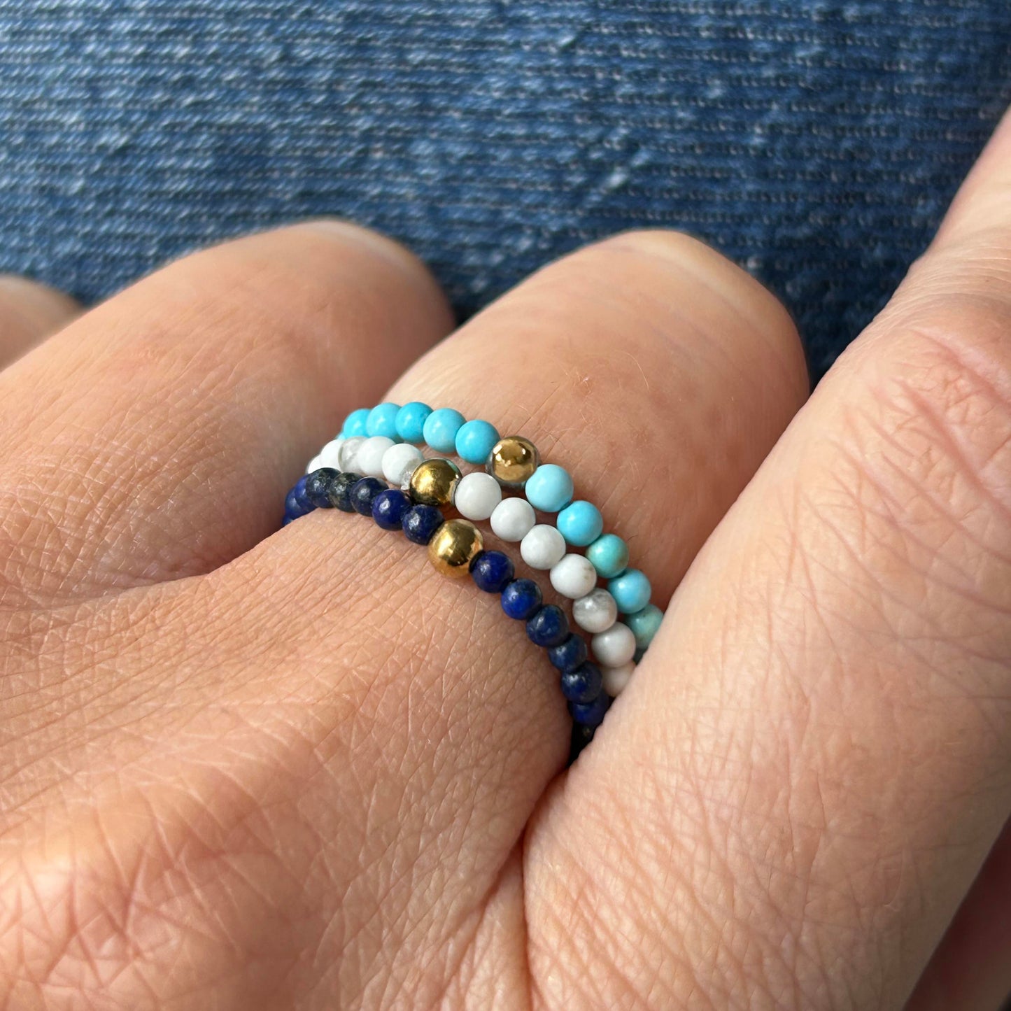Affordable stackable Aurora gemstone rings in turquoise, white and navy blue, styled on hand over denim.