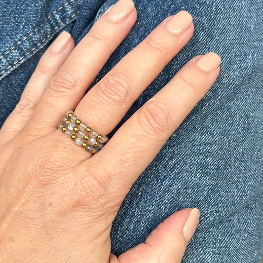 Affordable Leopoldine labradorite rings stacked on hand over denim, glowing with grey and gold tones.