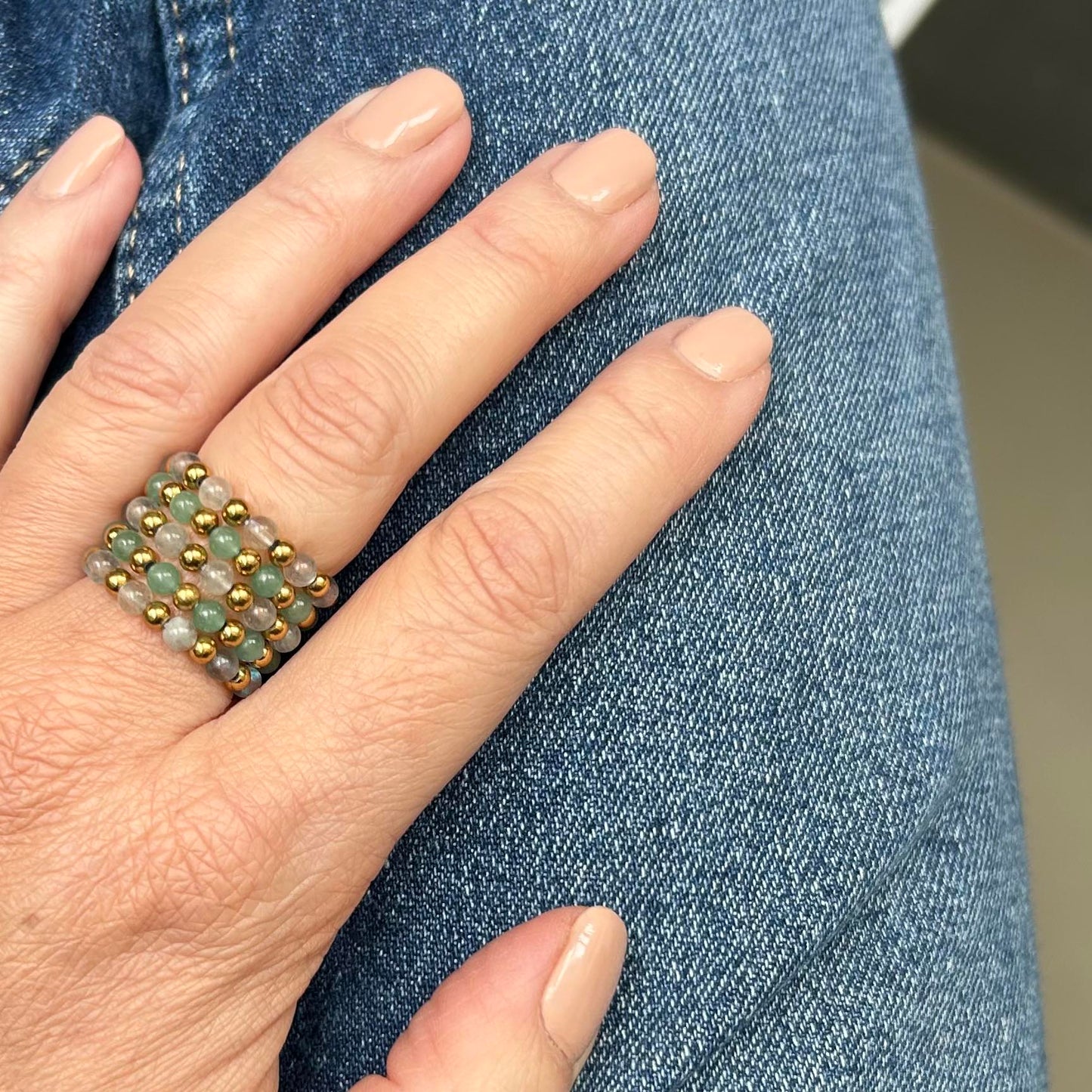 Affordable stack of Leopoldine Celestine rings with lapis lazuli, green and grey gemstones and gold-tone stainless steel, styled on hand over denim.