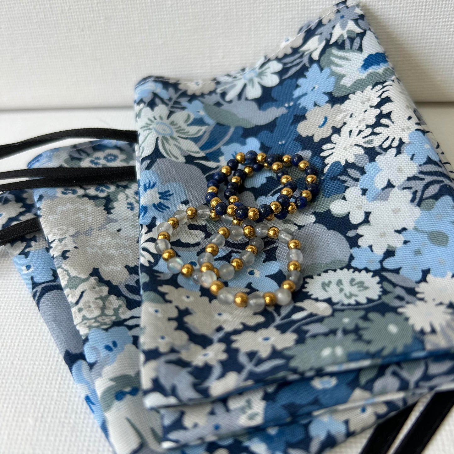 Bundle of affordable gold bead rings displayed on Liberty of London floral pouch in soft blue hues.