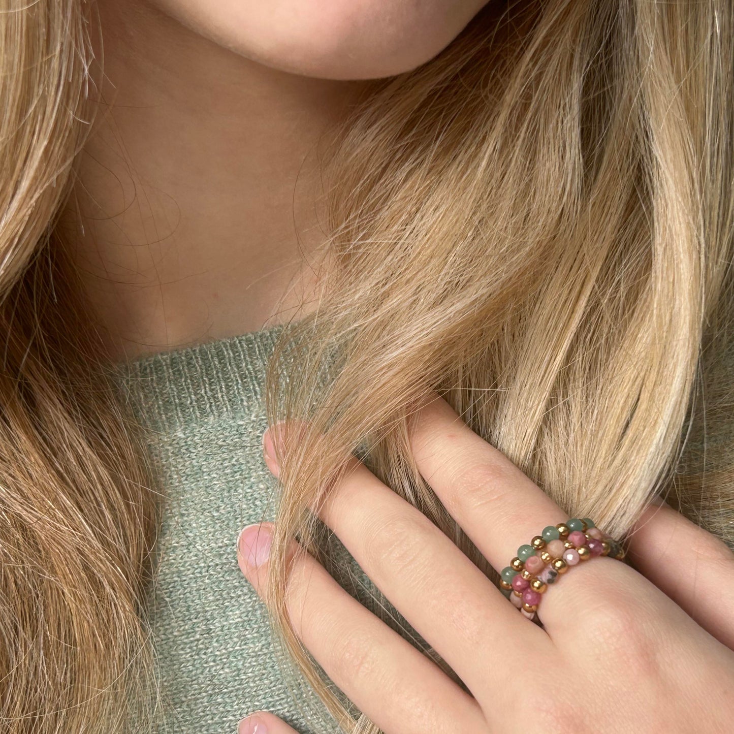 Affordable Leopoldine Celestine rings with pink and green gemstones and gold-tone stainless steel beads, styled on hand with pastel green knit.