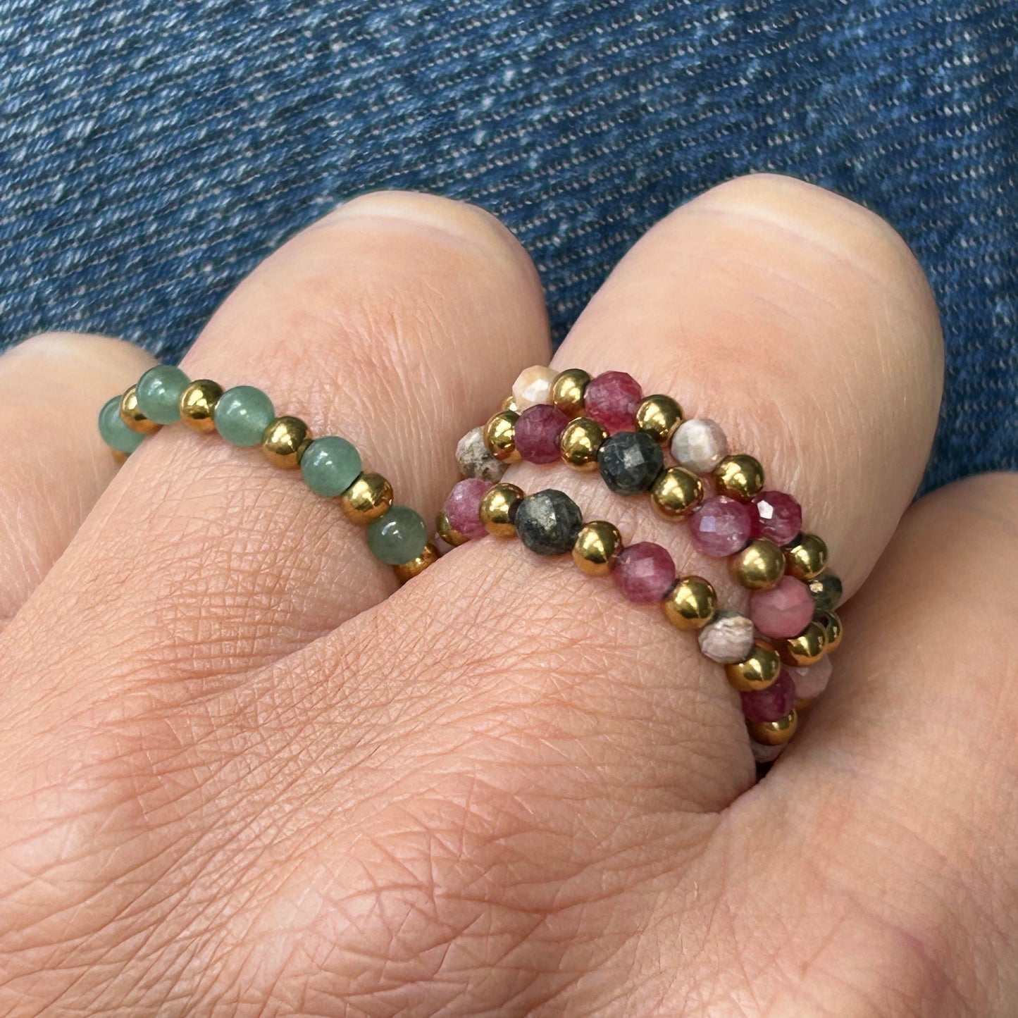 Affordable Leopoldine Celestine rings with rhodonite pink and green gemstones, paired with gold-tone stainless steel beads, styled on hand against denim.