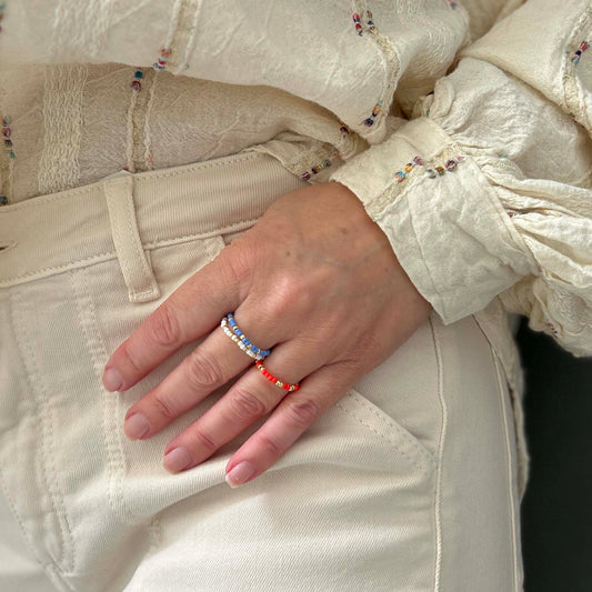 Leopoldine Confettis rings in blue, white and red glass beads with gold accents, stacked on fingers — playful UK jewellery set for a fun, colourful look.