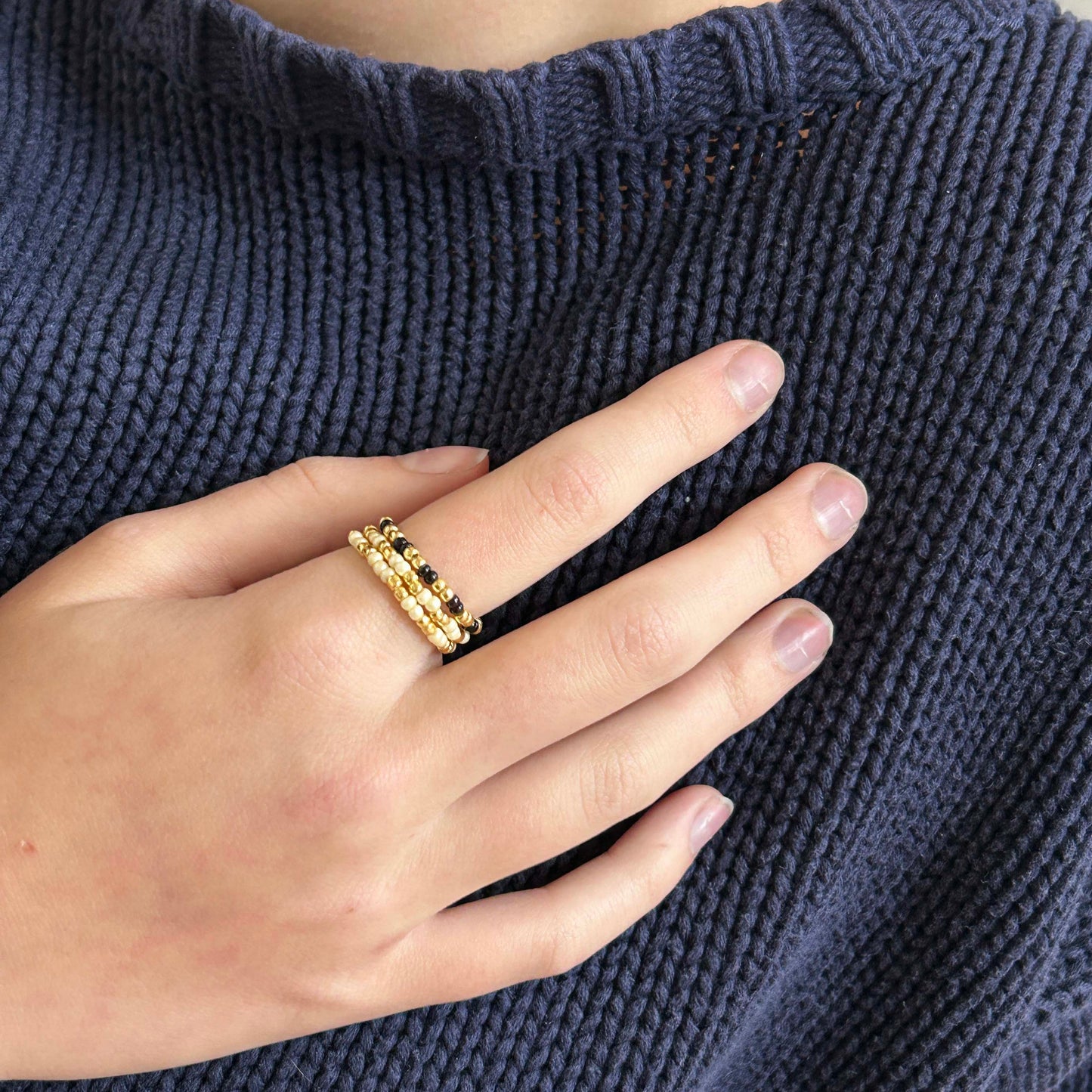 Hand wearing affordable Leopoldine Confettis cream and black beaded rings with gold details — a bold and elegant trio perfect for everyday stacking.