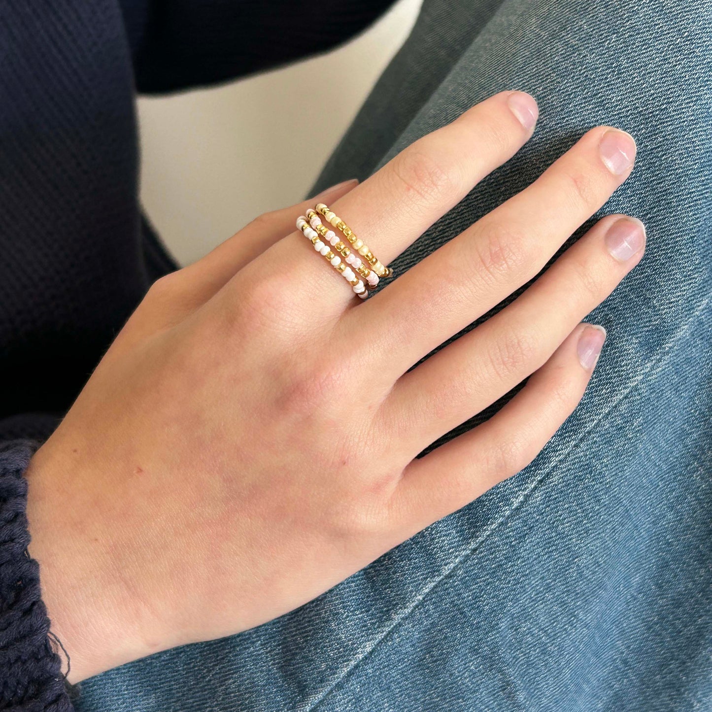 Hand wearing three stackable Leopoldine Confettis rings in cream, white, and pink glass beads with gold detailing — playful and chic jewellery for UK fashion lovers.