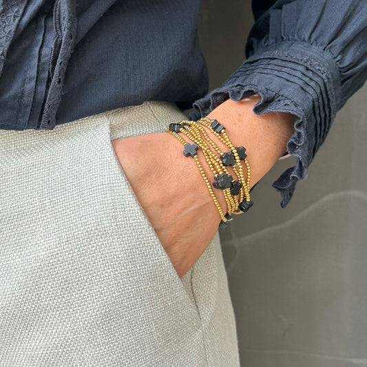 Elegant stack of gold and black cross bead bracelets on wrist. Chic UK jewellery with matte black crosses and shiny golden accents, perfect for stylish layering and everyday wear.