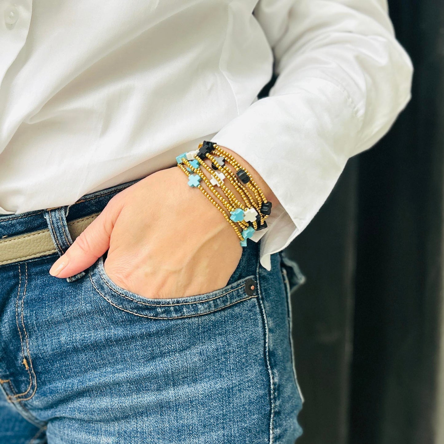 Wrist styled with Divine Cross bracelets in turquoise, white and black beads – stackable gold beaded jewellery, bold and adjustable for everyday layering.
