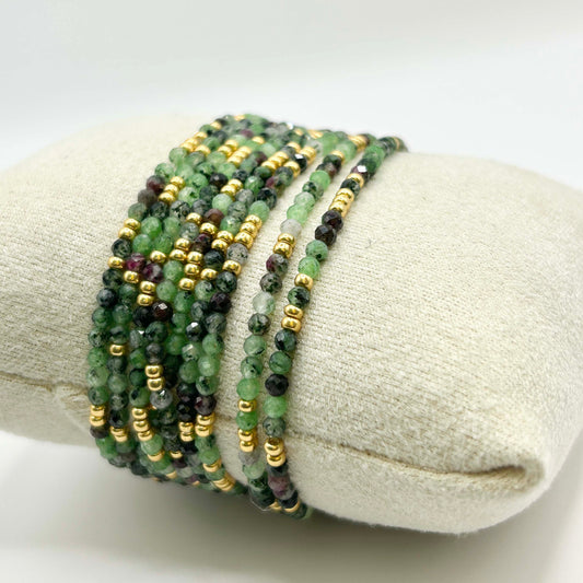 Close-up of the Leopoldine Selene bracelet in green gemstones and gold beads, elegantly coiled on a cream display cushion – luxurious yet earthy stackable jewellery.
