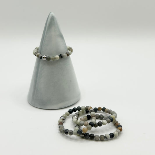 Grey Picasso gemstone stackable rings styled on a marble ring holder with extras laid flat beside.