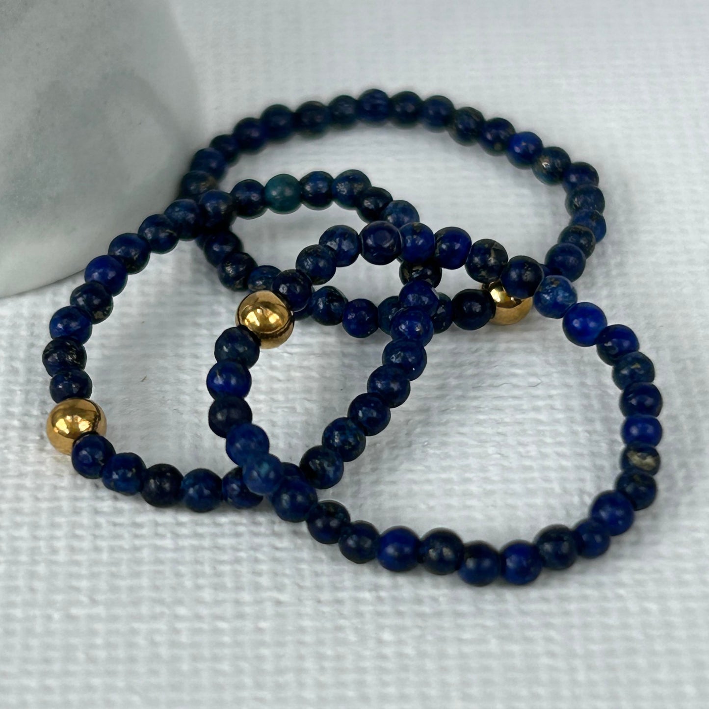 Set of stackable lapis lazuli rings with gold accents displayed on white fabric, perfect for layering jewellery lovers in the UK.