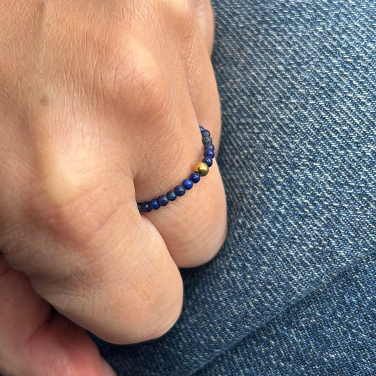 Minimalist lapis lazuli stackable ring with gold accents worn on finger, styled over denim for a casual-chic look.