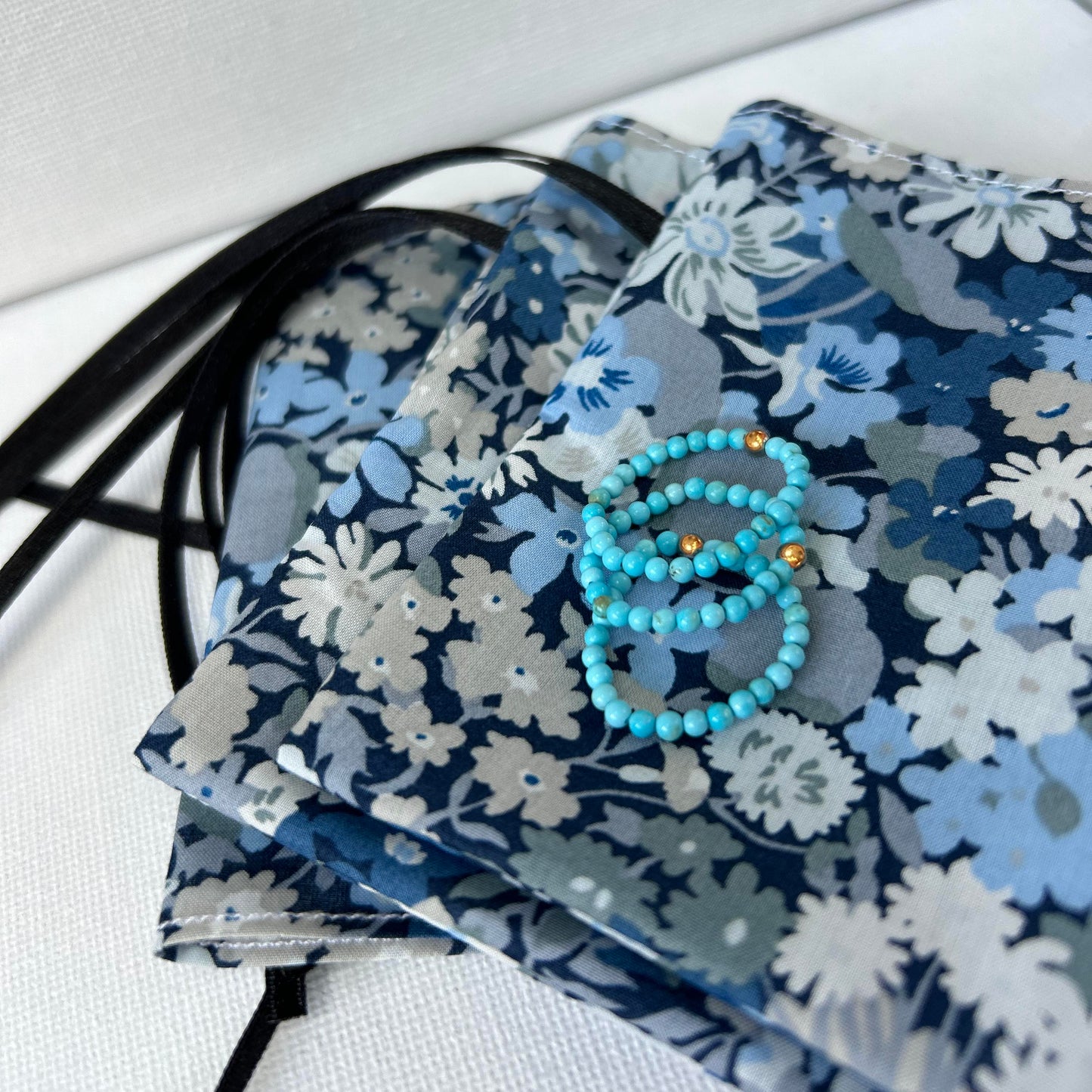Vibrant turquoise stackable rings with gold details, styled on a floral Liberty of London pouch – a playful jewellery gift idea UK.