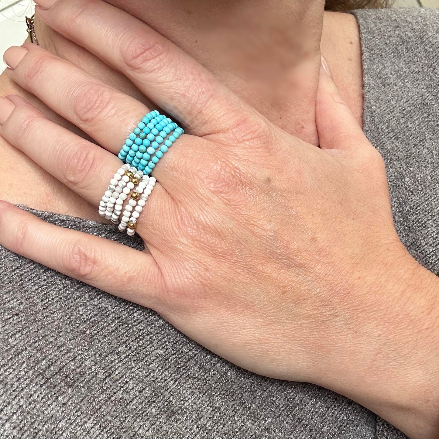 Stack of turquoise and white beaded rings styled on two fingers against a cosy grey top – stackable rings for her UK.