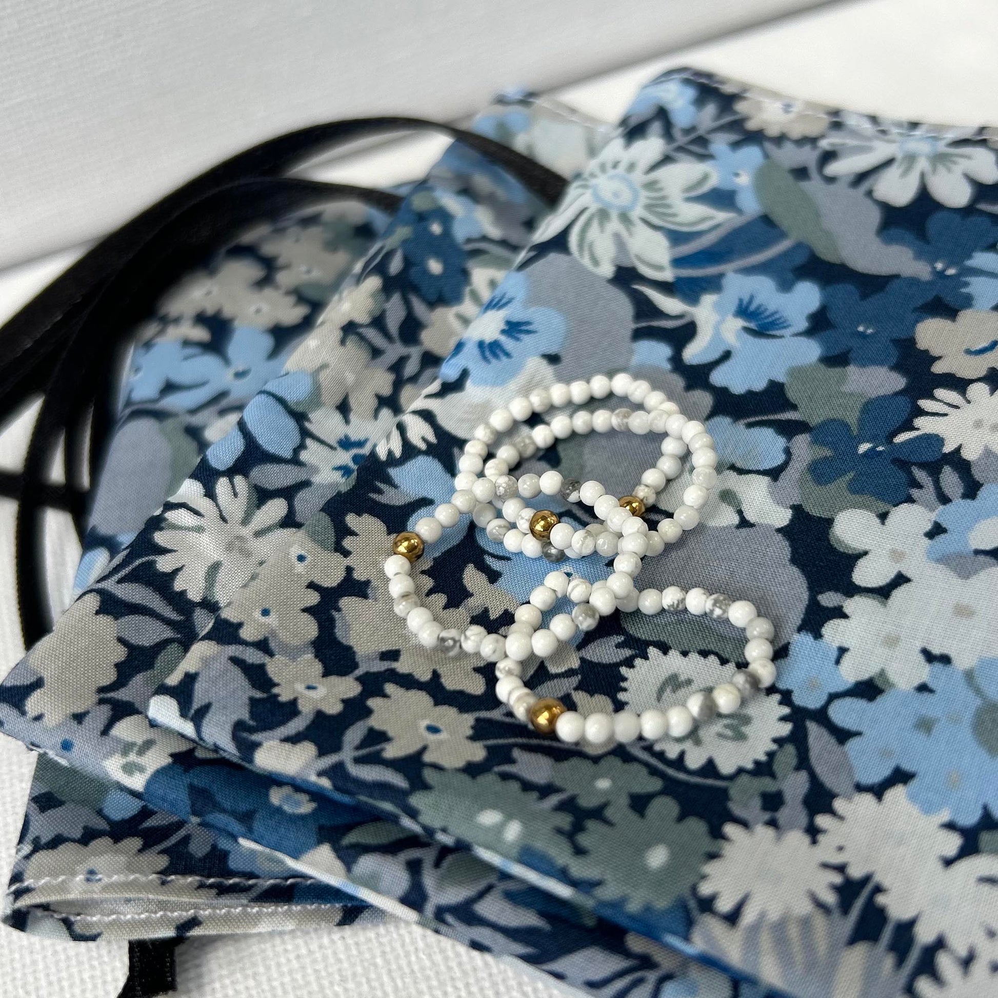 Affordable white beaded stackable rings with gold accents from Leopoldine, styled on a floral Liberty pouch – perfect for gifting UK jewellery lovers.