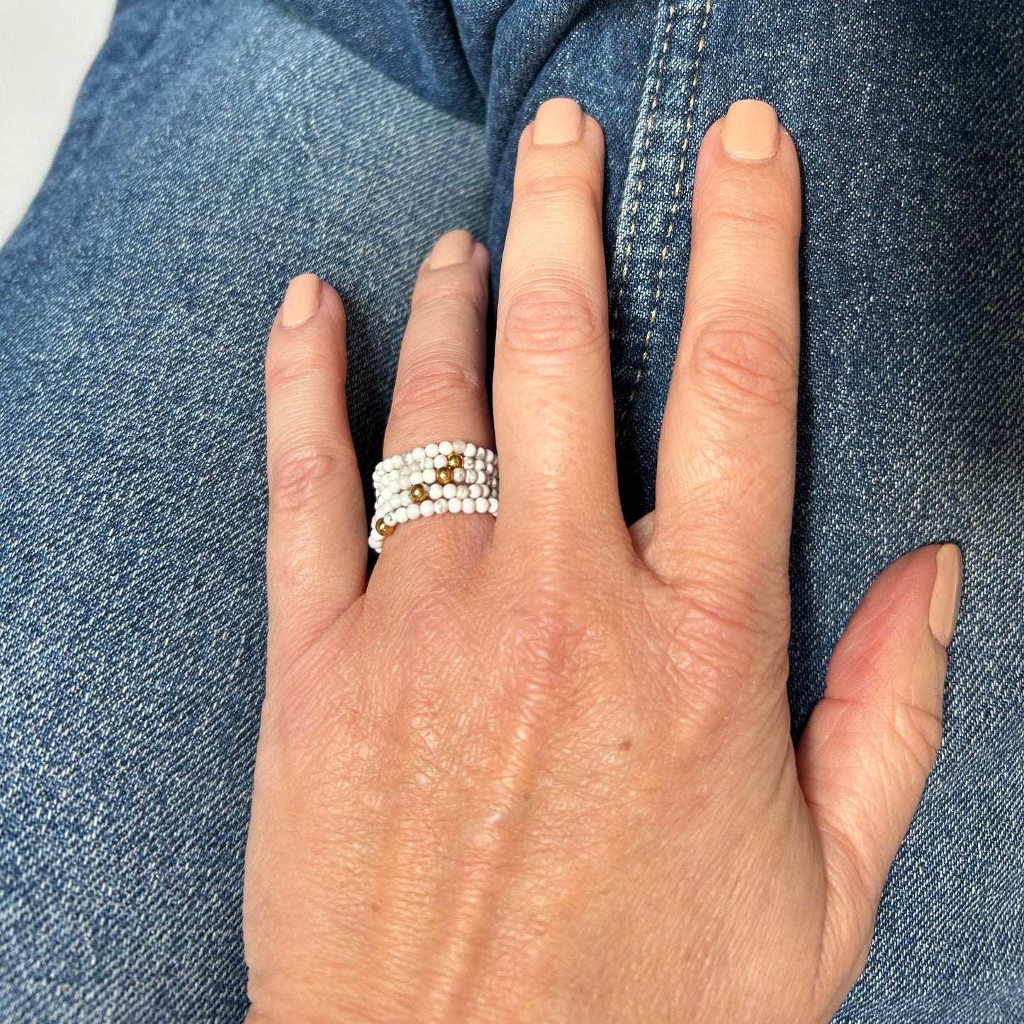Close-up of a hand wearing affordable white and gold stackable rings by Leopoldine, styled casually over denim – playful and elegant everyday jewellery UK.