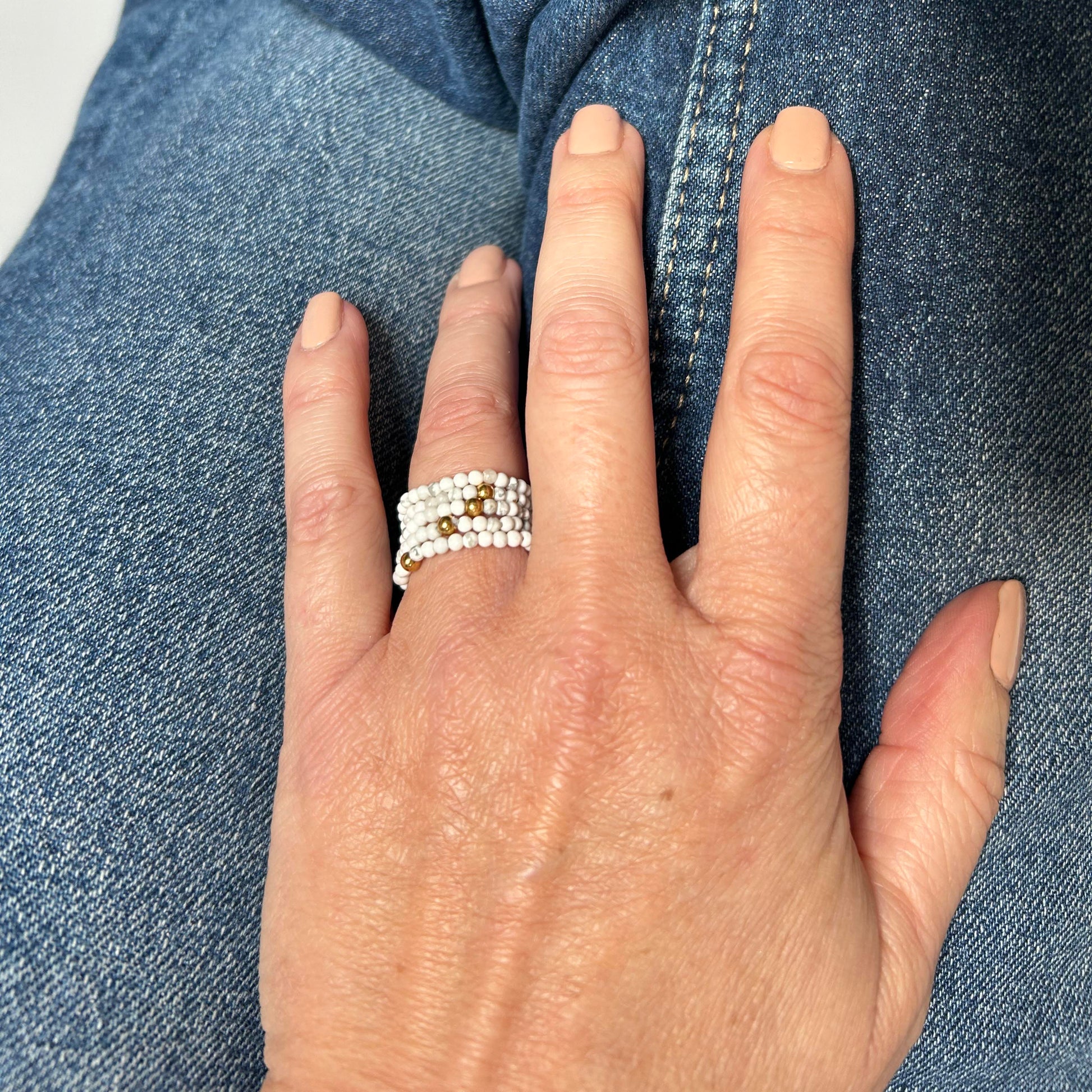 Close-up of a hand wearing affordable white and gold stackable rings by Leopoldine, styled casually over denim – playful and elegant everyday jewellery UK.