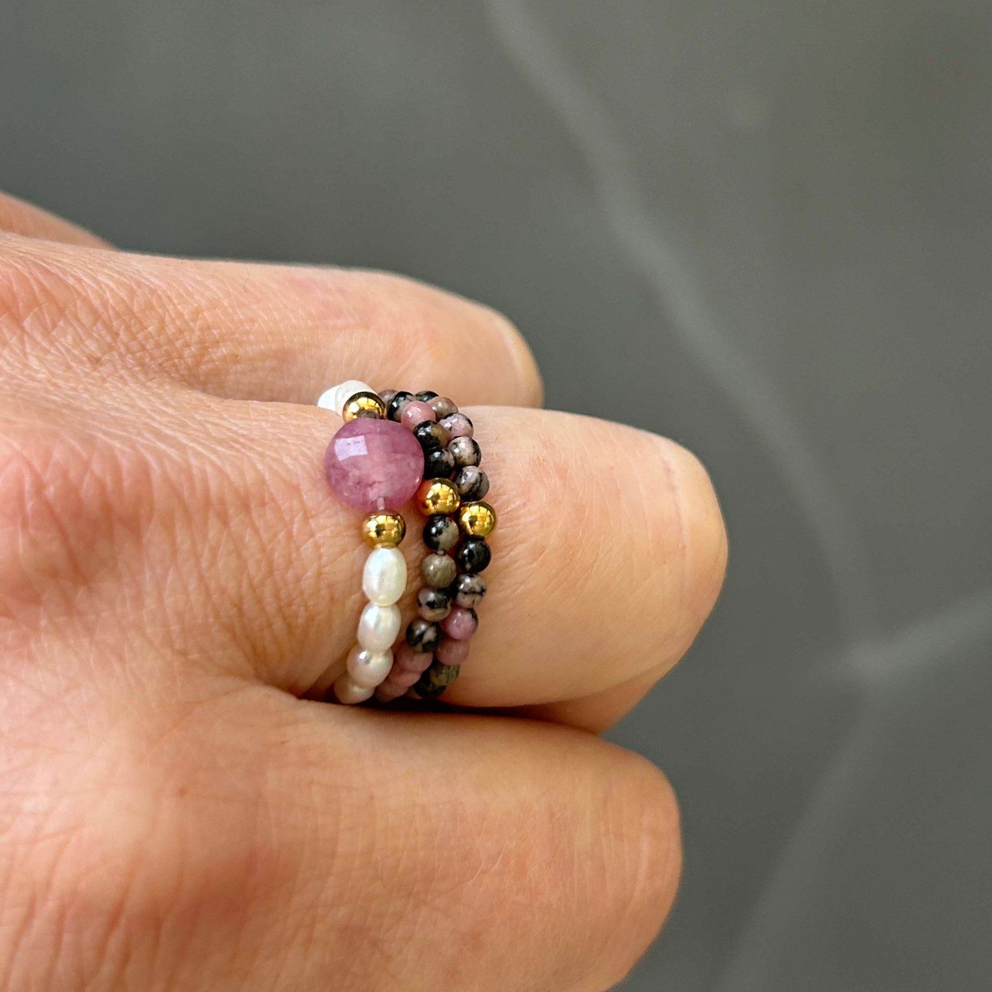 Detailed close-up of a trio stack ring featuring pink rhodonite, ivory pearls and gold stainless steel beads on a finger. Stylish UK minimalist jewellery with soft pink tones, perfect for layering or gifting.