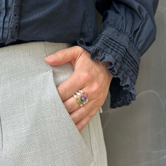 Elegant hand wearing a trio of beaded rings in pink tourmaline, green jade, and blue lapis lazuli. Colourful gemstone ring stack with pearls, perfect for a playful UK jewellery look with a timeless twist.