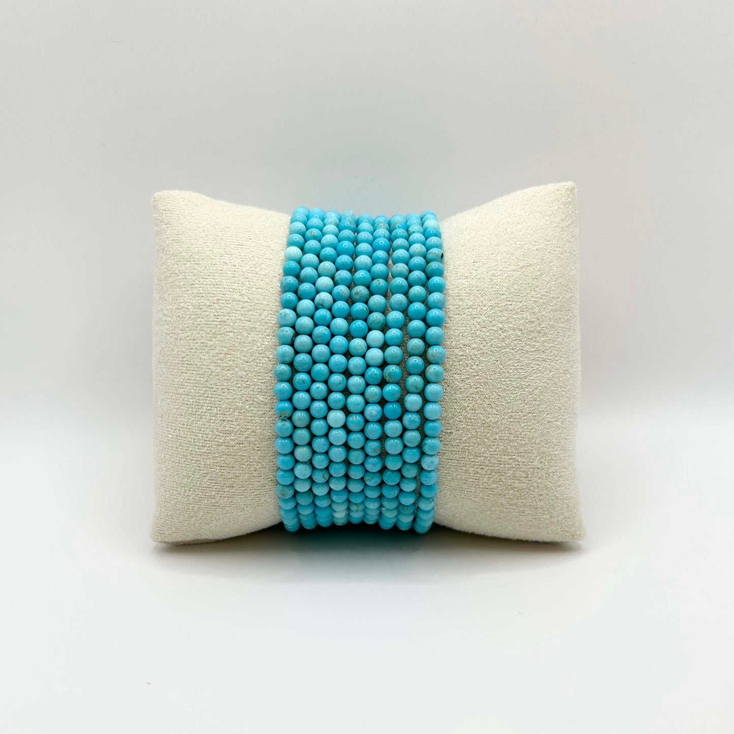 Affordable gemstone bracelet stack in vibrant turquoise – featuring smooth round beads perfectly aligned on a soft neutral cushion, ideal for creating a playful yet elegant wrist stack.