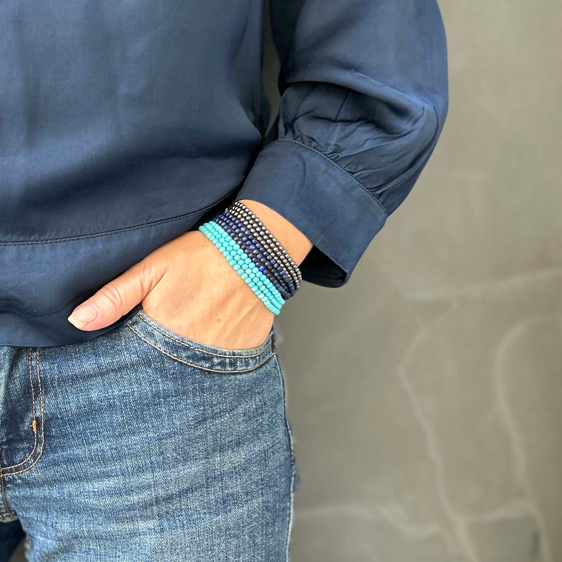 Wrist adorned with a stack of turquoise, lapis lazuli, and hematite bead bracelets – vibrant, layered gemstone accessories styled with a casual denim outfit.