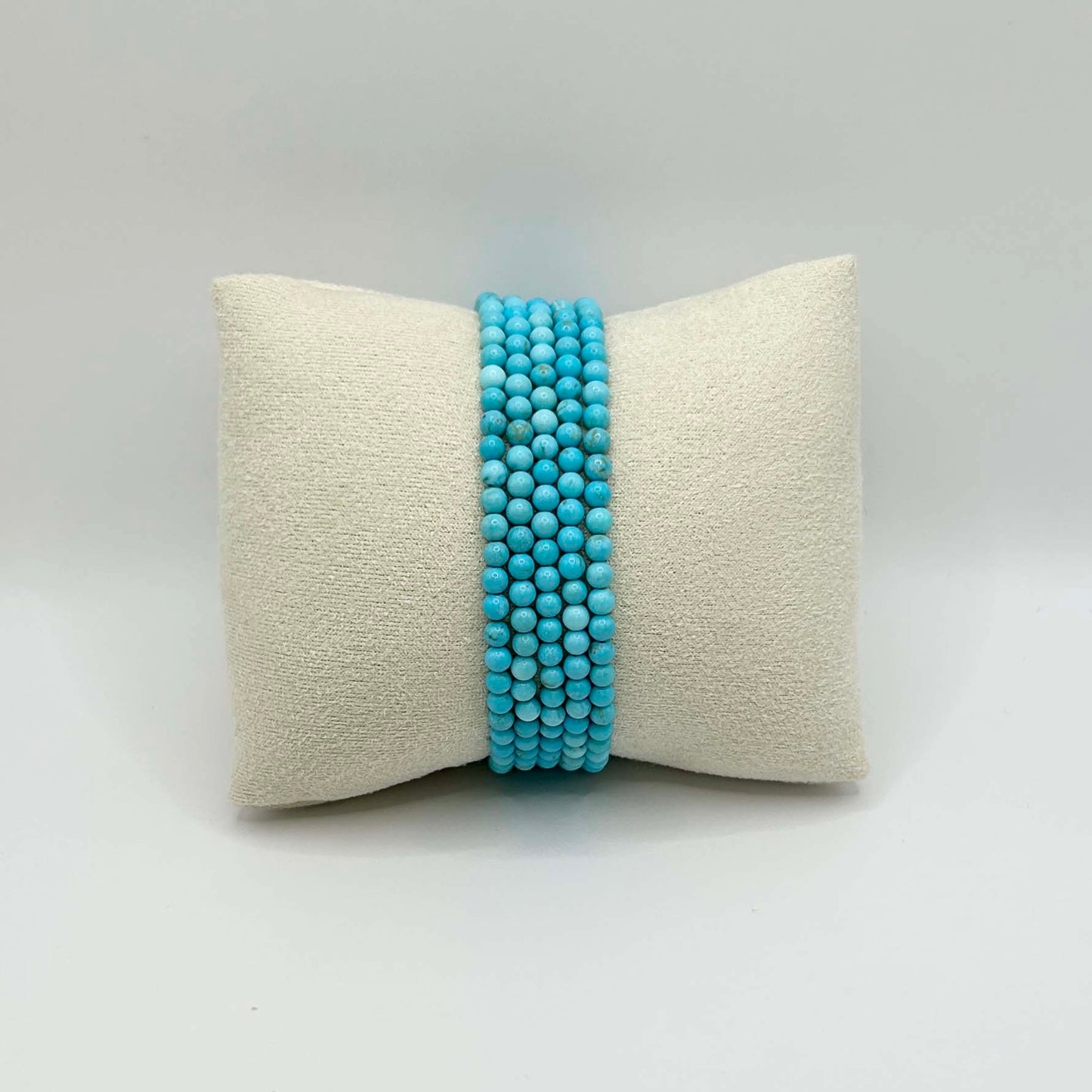 Affordable stack of turquoise Aurora bracelets displayed on a neutral cushion – elegant and minimalist gemstone jewellery perfect for layering or gifting.