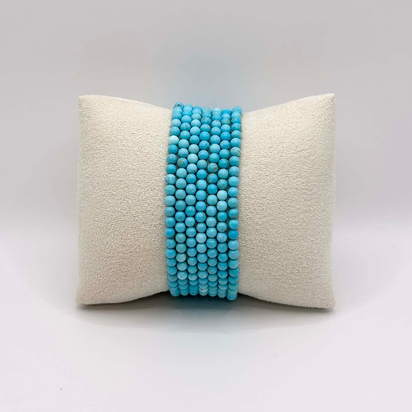Affordable stack of vibrant turquoise Aurora bracelets – bold and cheerful gemstone jewellery neatly arranged on a cream cushion, perfect for layering or wearing solo.