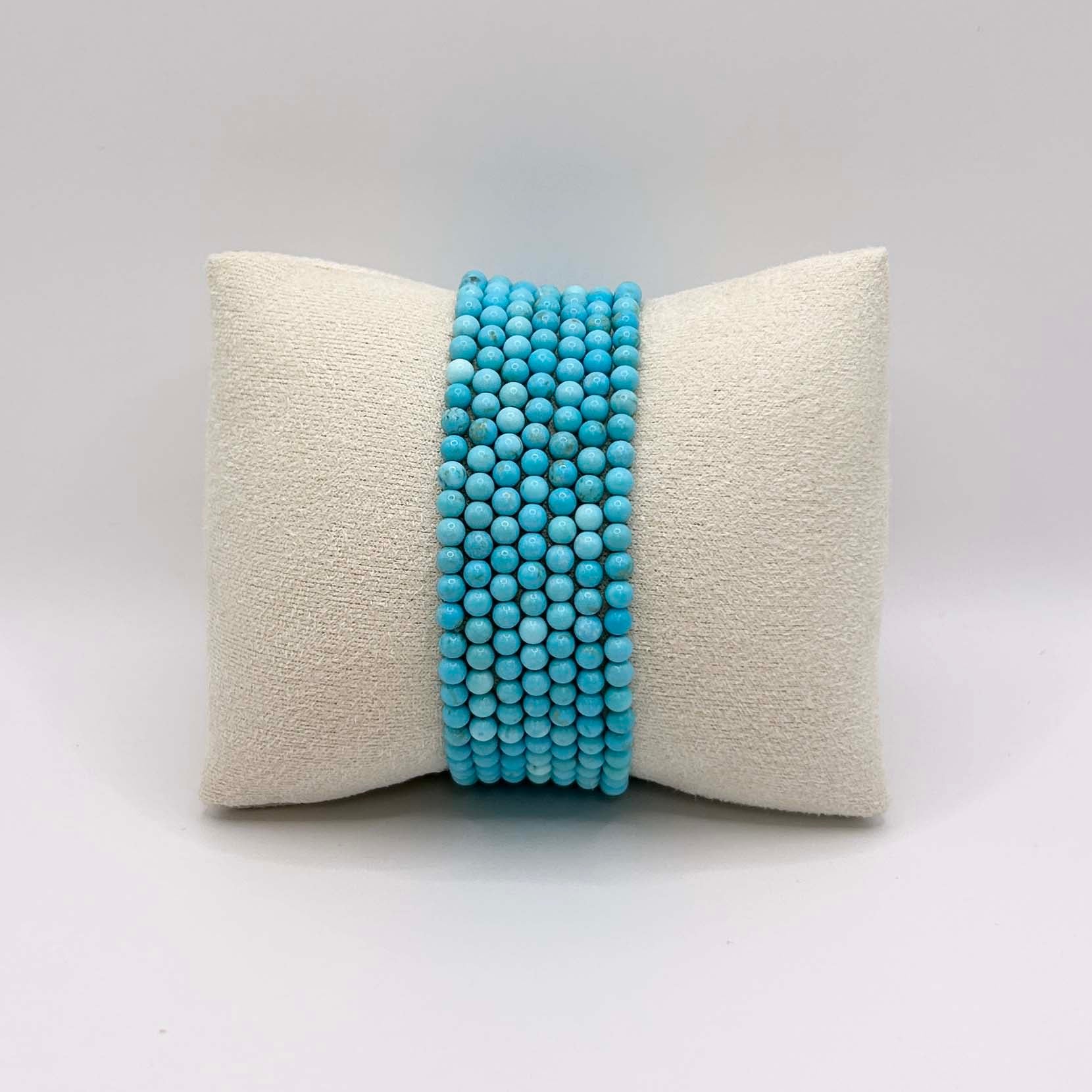 Affordable stack of vibrant turquoise Aurora bracelets – bold and cheerful gemstone jewellery neatly arranged on a cream cushion, perfect for layering or wearing solo.
