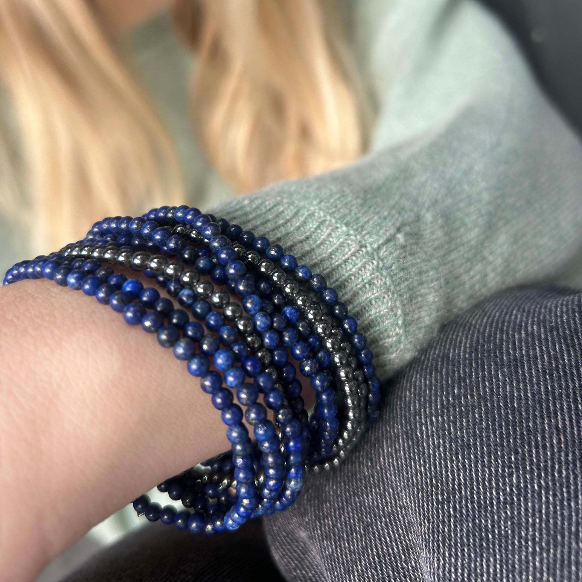 Woman wearing a stack of Leopoldine Aurora bracelets with deep blue lapis lazuli and shimmering hematite beads – bold, elegant and naturally magnetic.