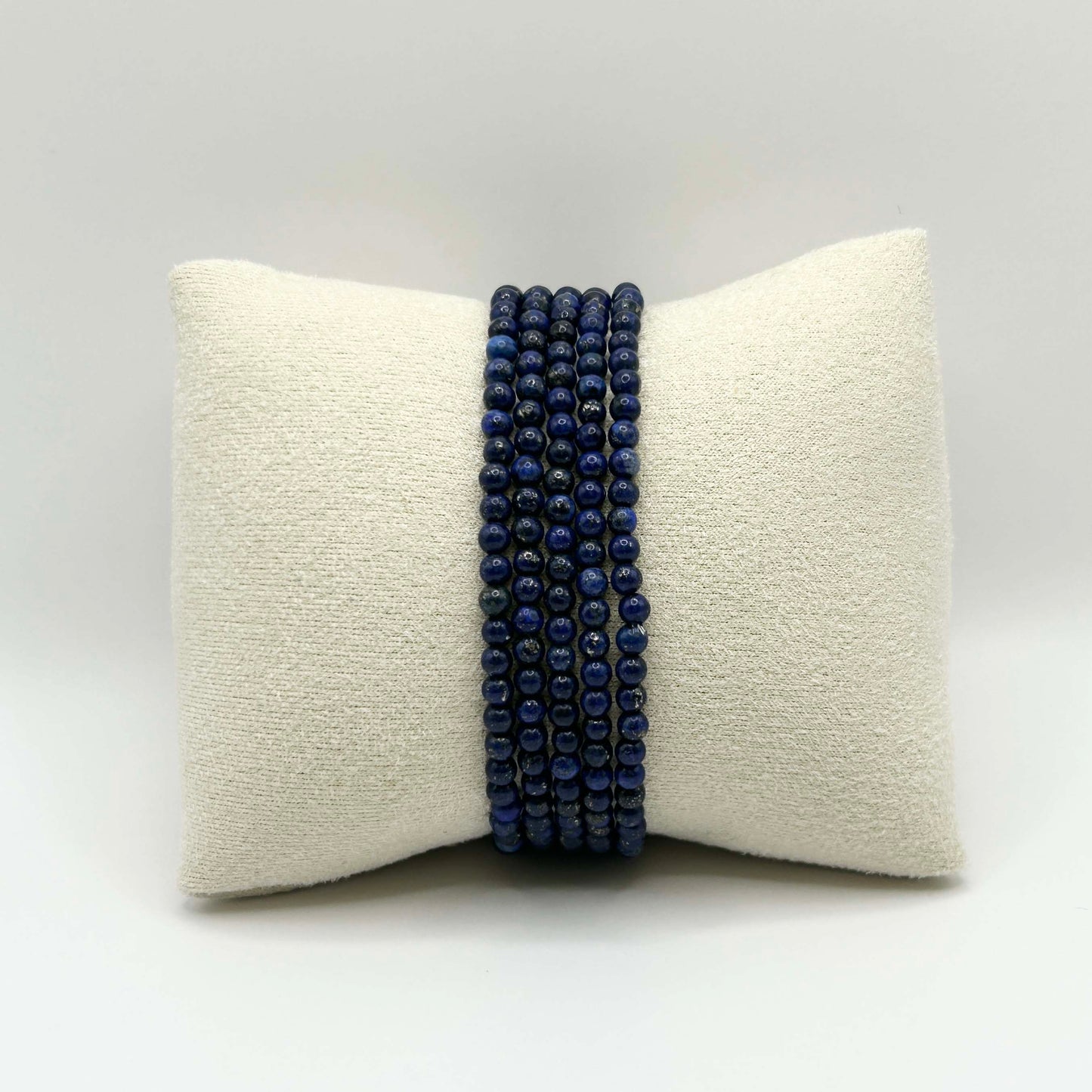 Lapis lazuli stacking bracelets arranged on a soft cream cushion – elegant deep blue beads for a timeless, boho-chic jewellery display.