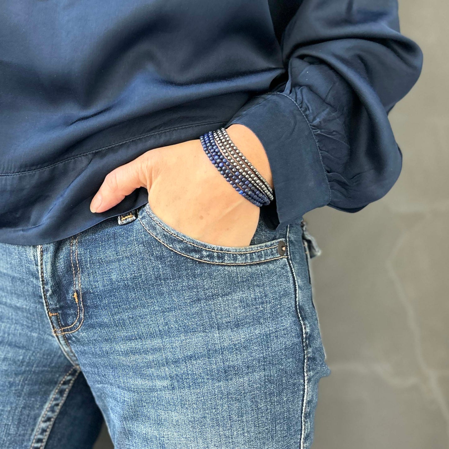 Close-up of wrist wearing stacked lapis lazuli and hematite beaded bracelets – styled casually with blue jeans and a navy sweatshirt for a relaxed yet polished look.