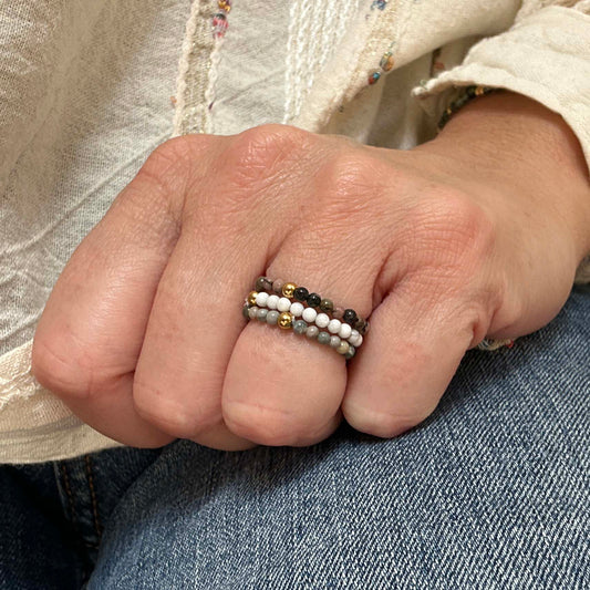 Close-up of a woman's hand wearing a stack of three beaded rings featuring white turquoise, grey Picasso jasper, and green flower jasper. Minimalist UK jewellery perfect for everyday wear and effortless styling.
