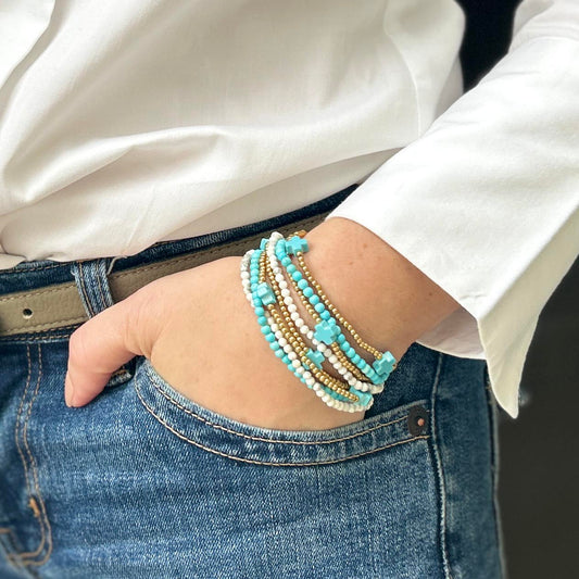 Wrist adorned with stackable Calypso turquoise and gold beaded bracelets – playful affordable jewellery, lightweight and perfect for layering.