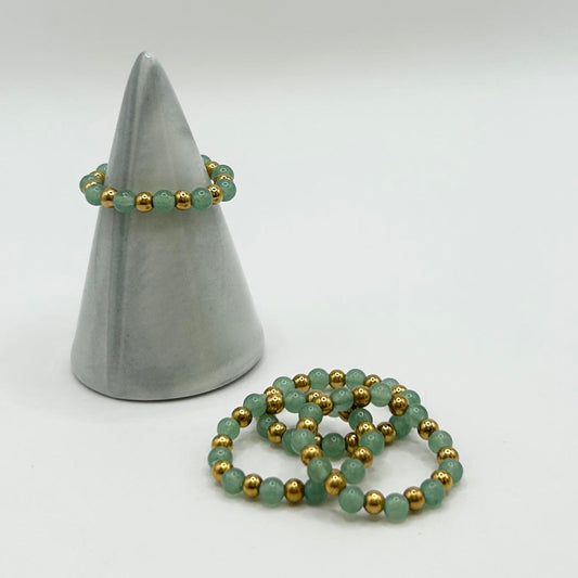 Affordable green aventurine ring with gold accents on ceramic cone, paired with extra stackable rings on white background.