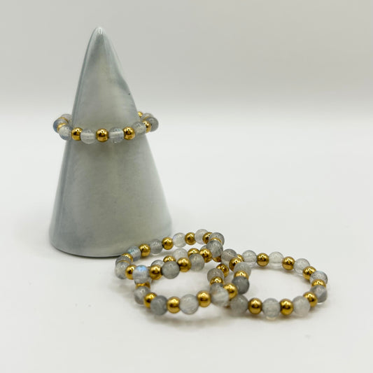 Affordable labradorite ring set from Leopoldine displayed on cone stand, showing grey gemstone shimmer and gold accents.