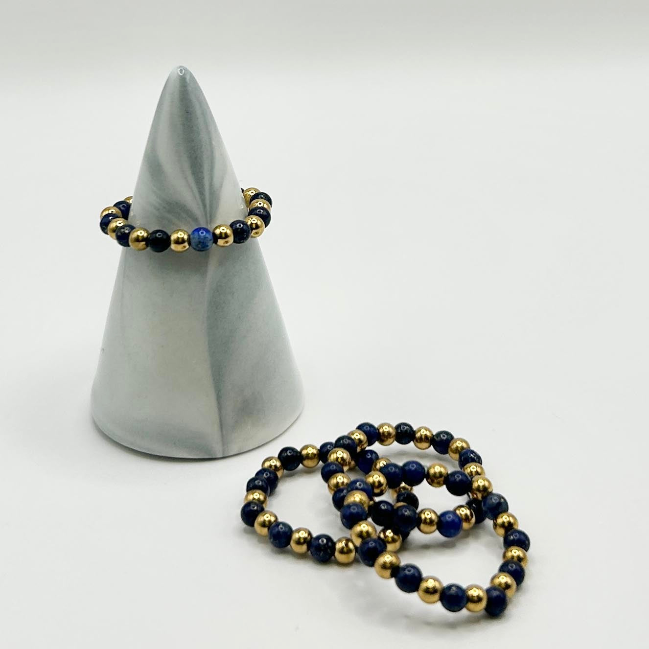 Close-up of gold and lapis lazuli ring styled on marble cone, paired with stacked designs beside it.