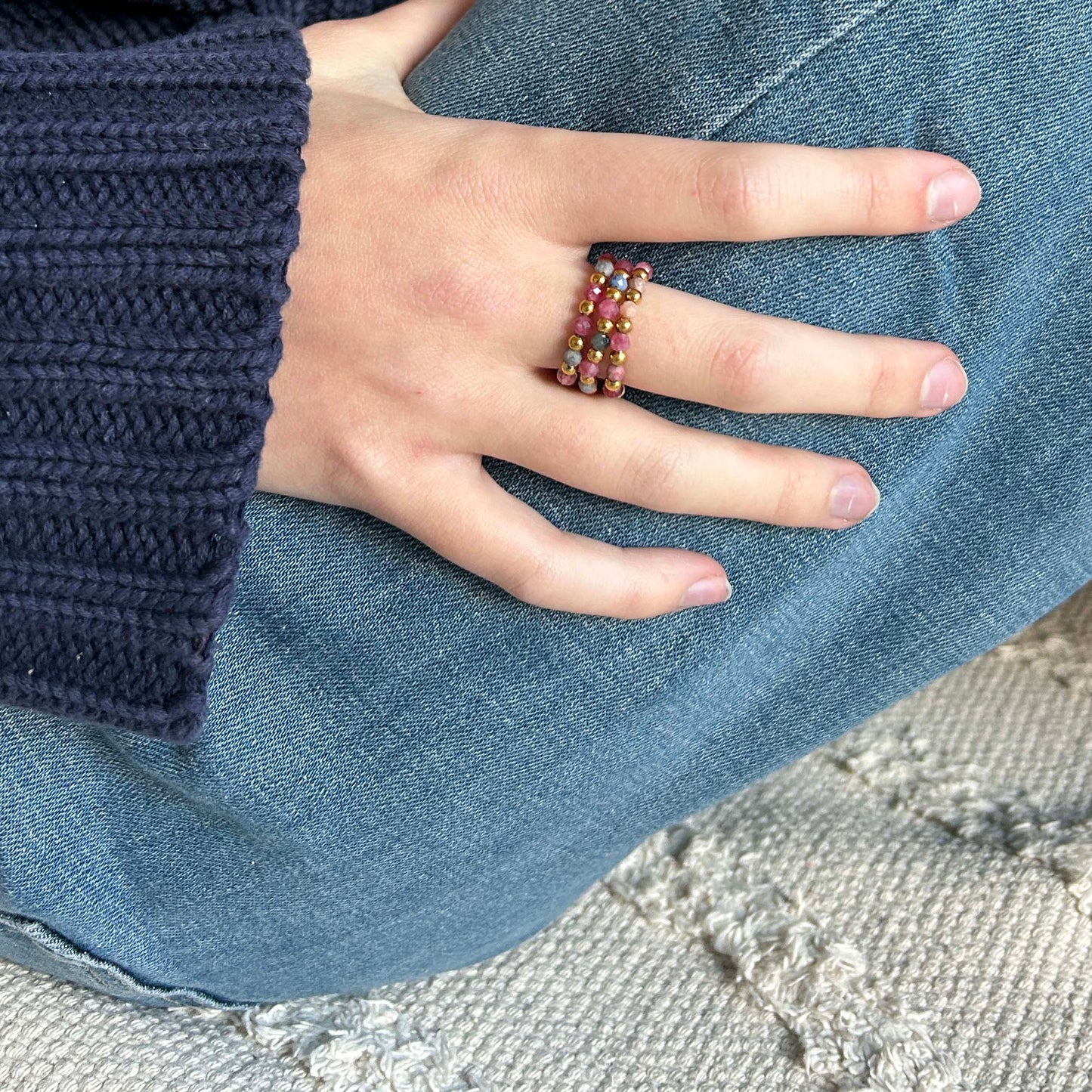 Leopoldine Celestine ring trio in pink tones with gold accents, styled on hand over denim and a navy knit — a colourful, affordable jewellery set for playful everyday styling.