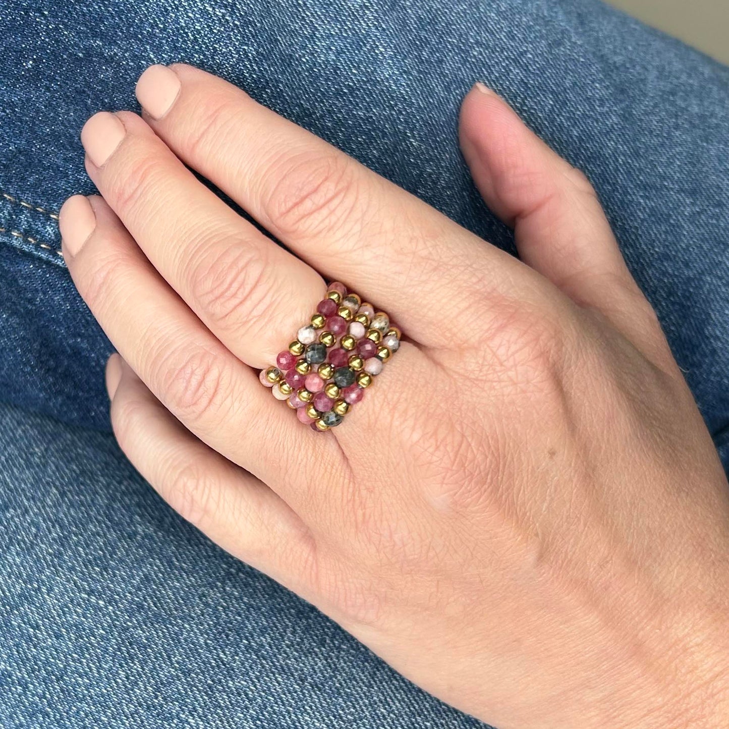 Hand wearing affordable Leopoldine stackable rings with pink rhodonite beads and gold detailing on denim backdrop.