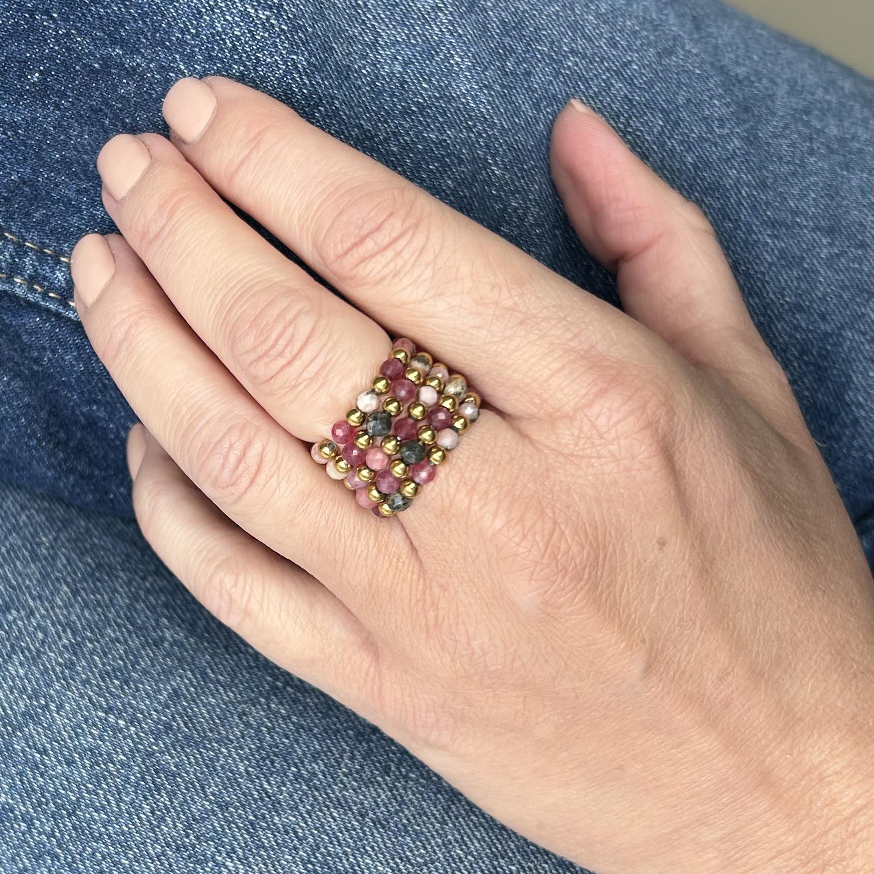 Hand wearing affordable Leopoldine stackable rings with pink rhodonite beads and gold detailing on denim backdrop.
