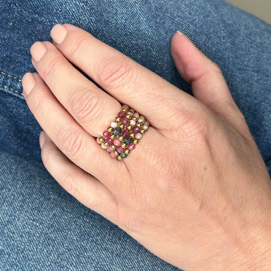 Hand wearing affordable Leopoldine stackable rings with pink rhodonite beads and gold detailing on denim backdrop.