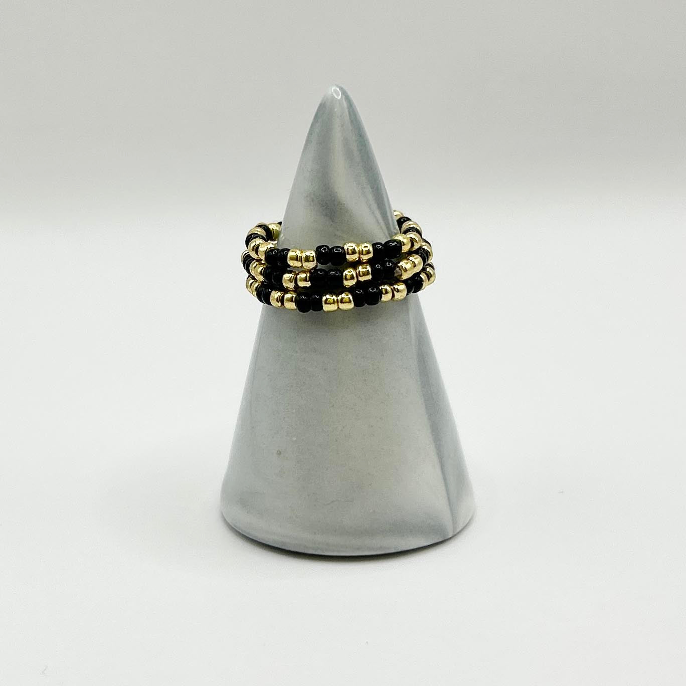Leopoldine Confettis trio rings in black and gold glass beads, displayed on a sleek grey cone for a bold look.