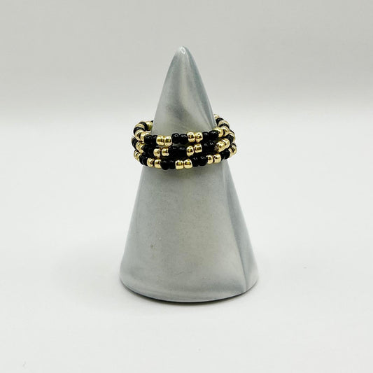 Leopoldine Confettis trio rings in black and gold glass beads, displayed on a sleek grey cone for a bold look.