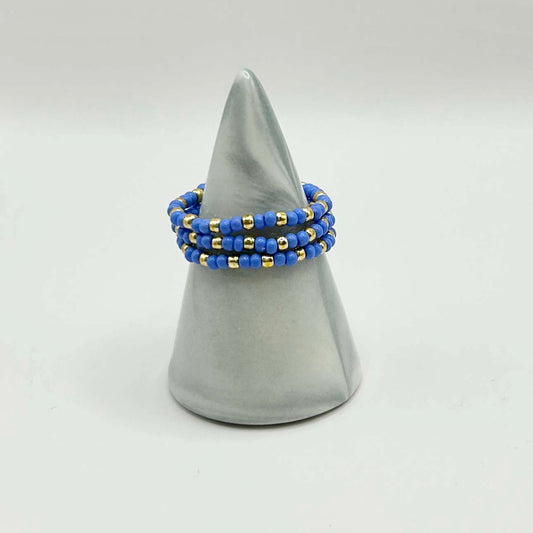 Leopoldine Confettis trio ring set with blue glass and gold beads, displayed on a grey cone stand — vibrant stackable jewellery for UK style lovers.