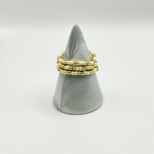 Trio of Leopoldine ivory Confettis rings with gold and pearl beads, styled on a minimalist grey cone display.