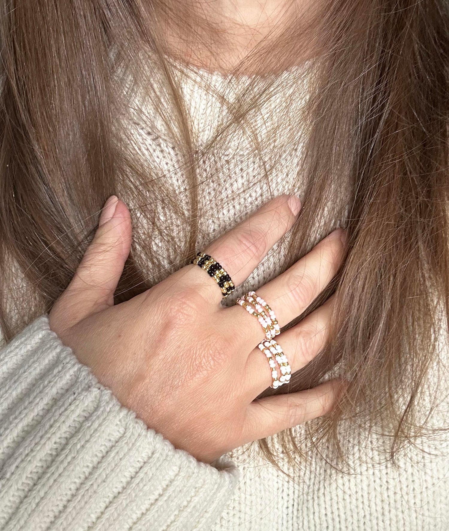 Hand wearing stacked affordable black and baby pink Leopoldine Confettis rings, styled with a cosy cream knit jumper – perfect for playful ring layering vibes.