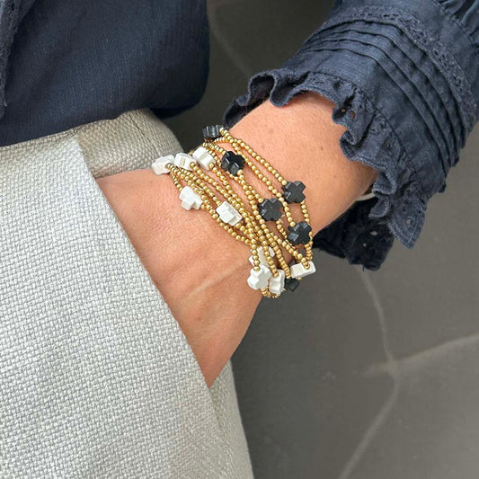 Stacked Divine cross bracelets in black and white with gold beads – minimalist jewellery for everyday wear, perfect wrist layering style. UK jewellery brand.